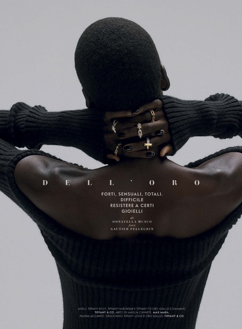 A person with dark skin and a shaved head is seen from behind wearing a black turtleneck sweater and rings on their fingers.
