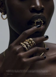 Close-up of model Nyawargak Gatluak wearing gold and diamond rings, with black nail polish and a ring held in her mouth.