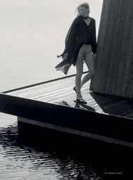 Monochrome fashion editorial image of a model standing on a wooden dock by the water for Vanity Fair Italia