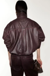 Model seen from behind wearing an oversized dark burgundy leather jacket and matching pants against a white background