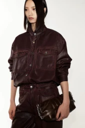 Model Huijia Chen wearing a dark burgundy buttoned jacket and matching trousers holding a dark handbag against a white background