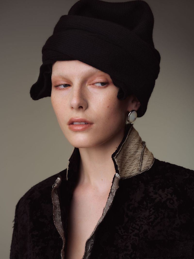Portrait of a fair-skinned woman with a black wrapped head covering, wearing large round earrings and a high-collared black brocade jacket.