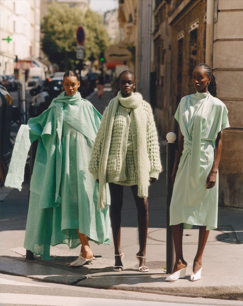 Three Black female fashion models in mint green outfits pose on a city street with cars and buildings in the background. Fashion shoot.