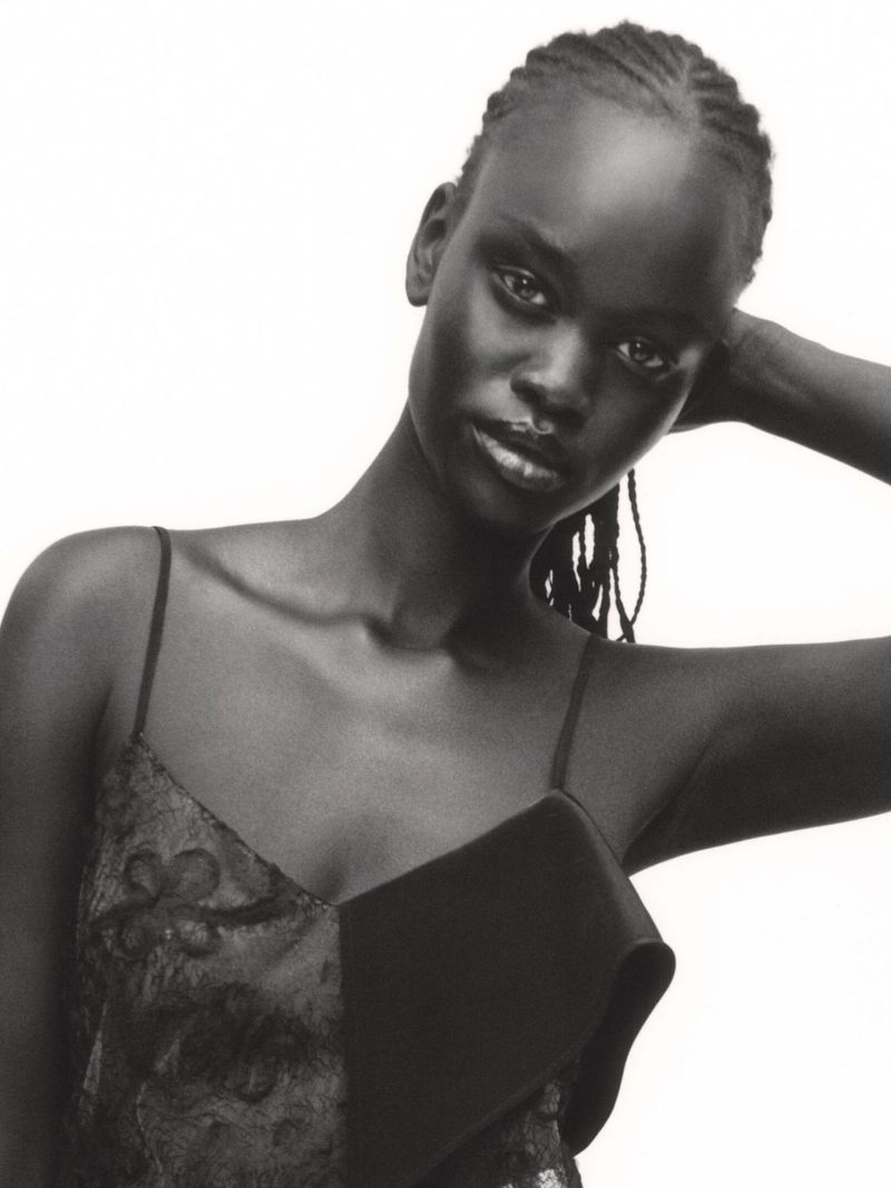 Black and white portrait of a Black female fashion model with braided hair, wearing a dress against a white backdrop in studio lighting.