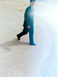 Model wearing a black suit walking across an outdoor paved public square with bright light flare.