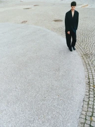 A person wearing a black suit walks across a paved outdoor square viewed from a high angle.