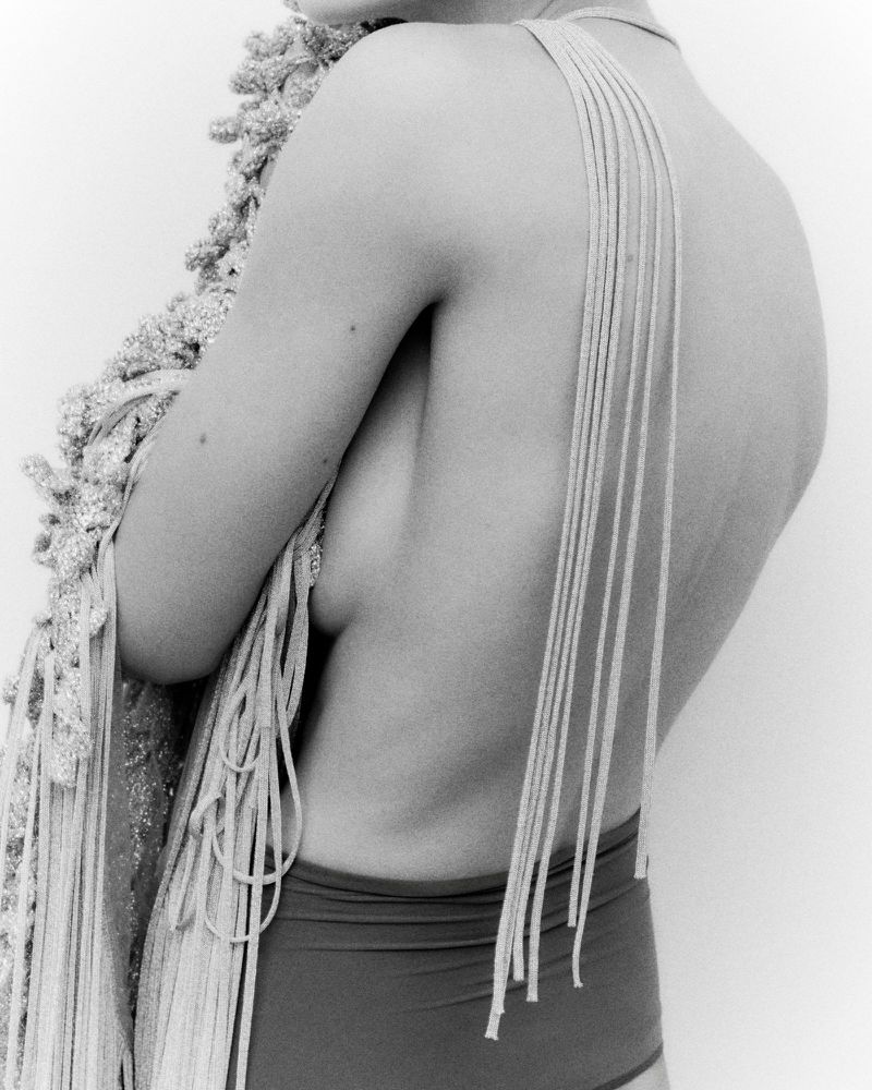 Black and white image of an adult female wearing a macrame style shawl, and briefs against a plain white background.