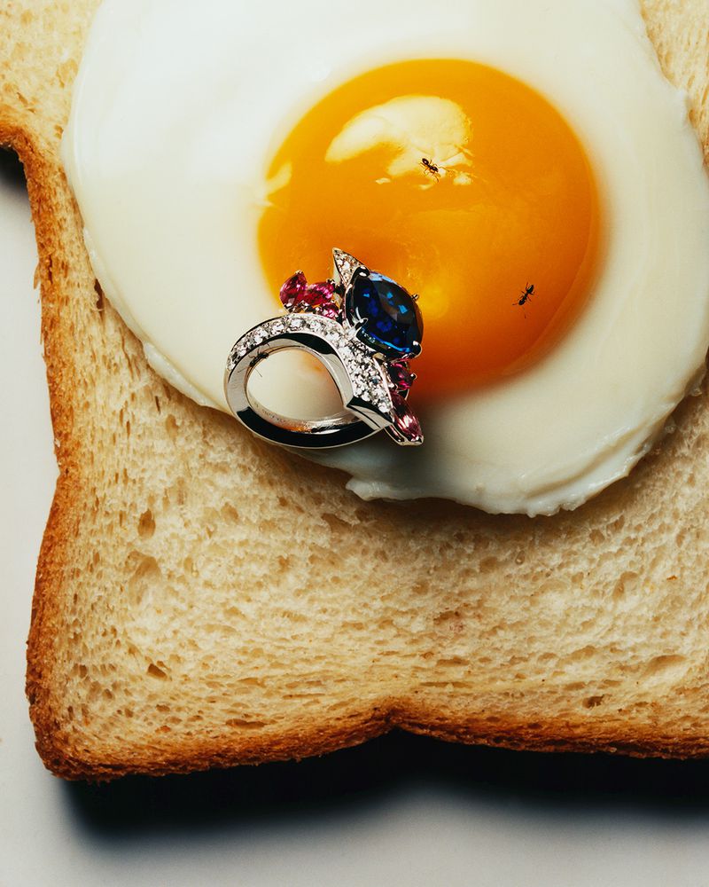 Jeweled ring with blue gem sitting atop a fried egg on a piece of toast, food and jewelry still life, high-angle, studio lighting.