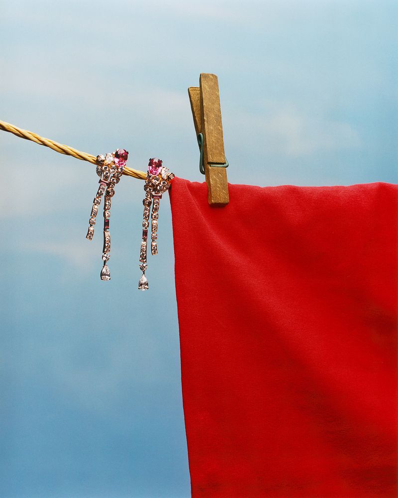 Elegant crystal dangle earrings sparkle on a clothesline beside a red garment against a bright blue sky, capturing beauty and simplicity.