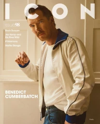 Benedict Cumberbatch wearing a white zip-up jacket with blue trim against a wood-paneled interior background.