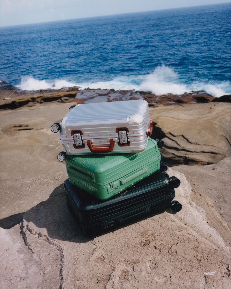 Three colorful suitcases stacked on a rocky beach with a blue ocean backdrop, creating a travel-themed, vibrant, and outdoor scene.