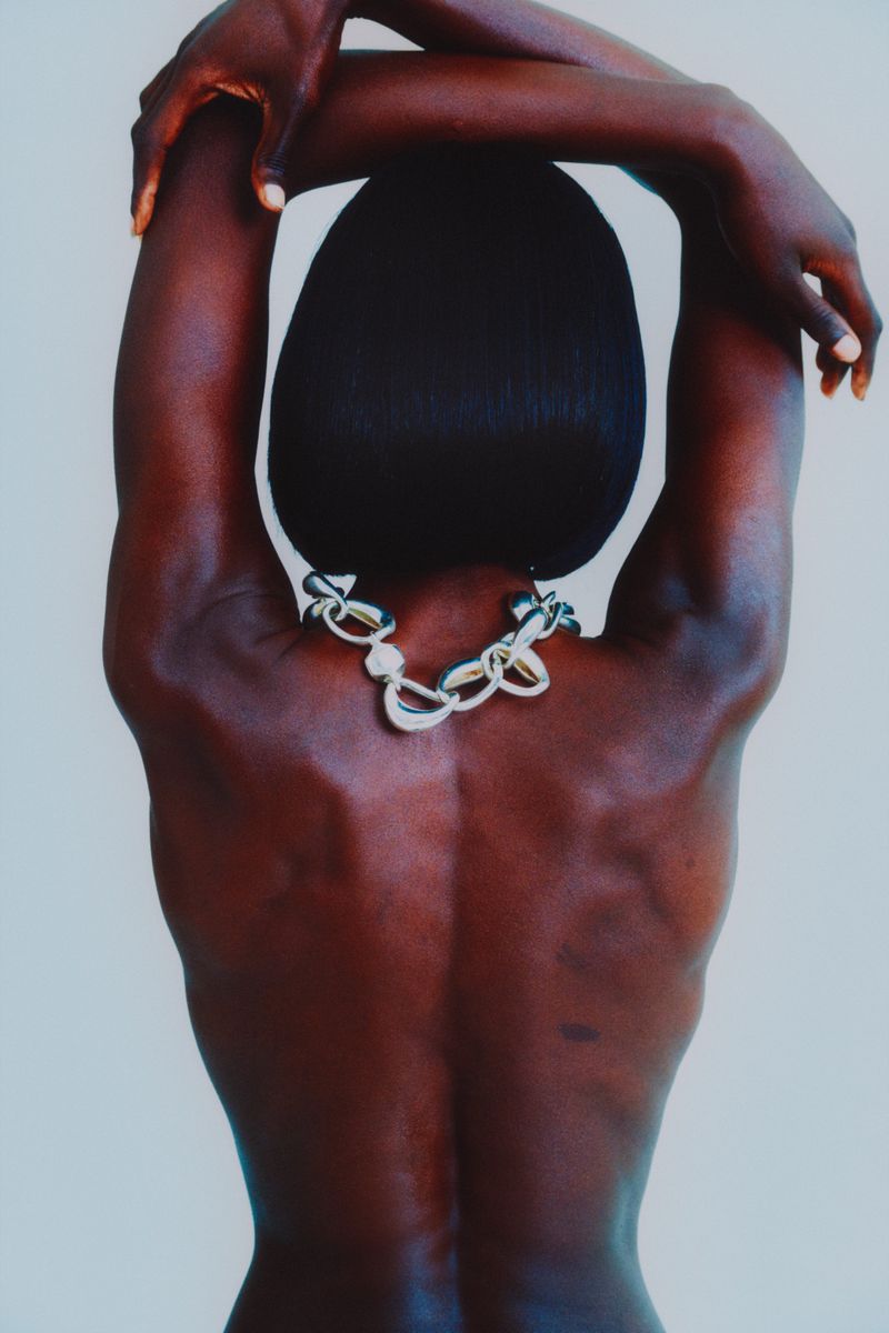 Close-up studio shot of an African-American female with her arms up and hands behind her head, wearing a silver chain necklace.