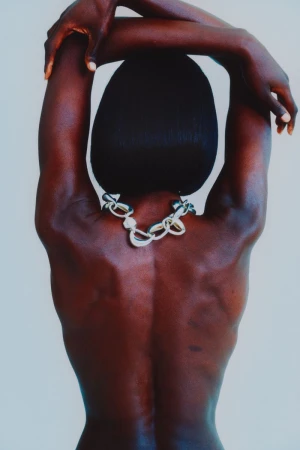 Close-up studio shot of an African-American female with her arms up and hands behind her head, wearing a silver chain necklace.