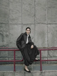 Model in a black leather jacket and long skirt posing against a textured stone wall