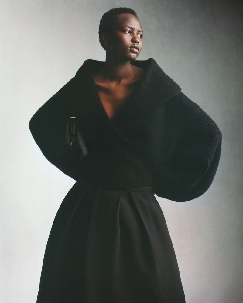 Elegant woman poses in a black wrap sweater and skirt against a neutral background in a fashion studio setting, medium shot.