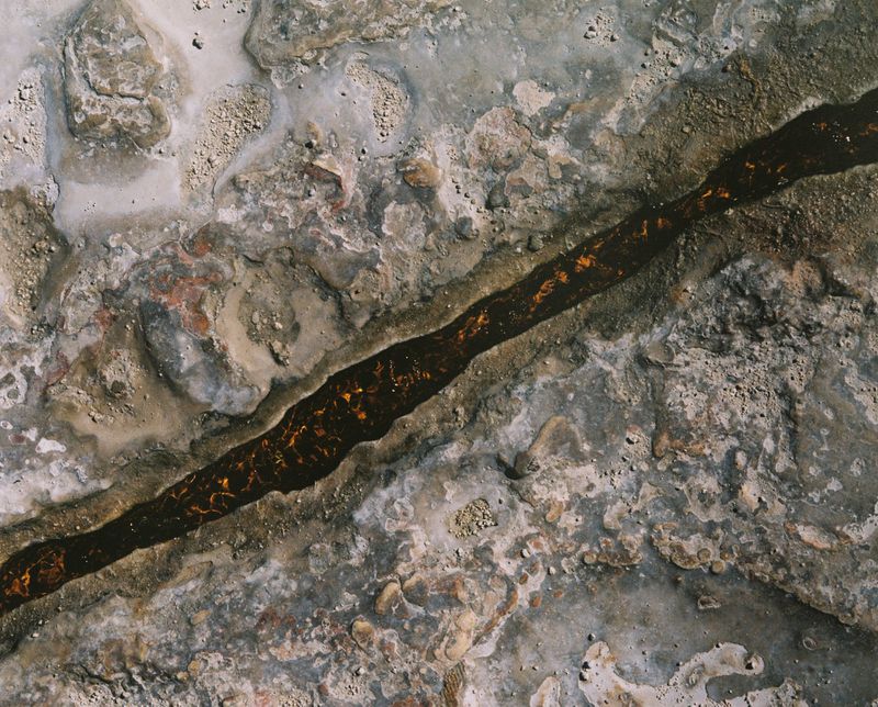 Abstract overhead shot of a dark brown liquid stream running through a textured grey and white stone surface, creating an earthy background.
