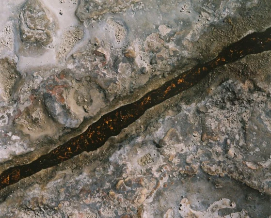 Abstract overhead shot of a dark brown liquid stream running through a textured grey and white stone surface, creating an earthy background.