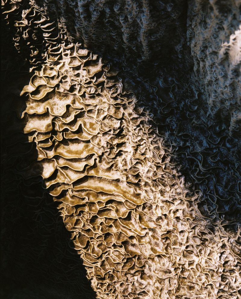 Abstract aerial photograph of intricate, curving patterns in rock formations, featuring light and shadow contrast and natural textures.