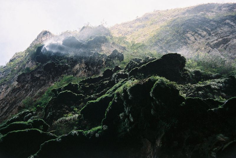 Lush green moss-covered rocks and a cascading waterfall on a mountainside, creating a natural and serene outdoor environment.