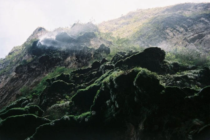 Lush green moss-covered rocks and a cascading waterfall on a mountainside, creating a natural and serene outdoor environment.
