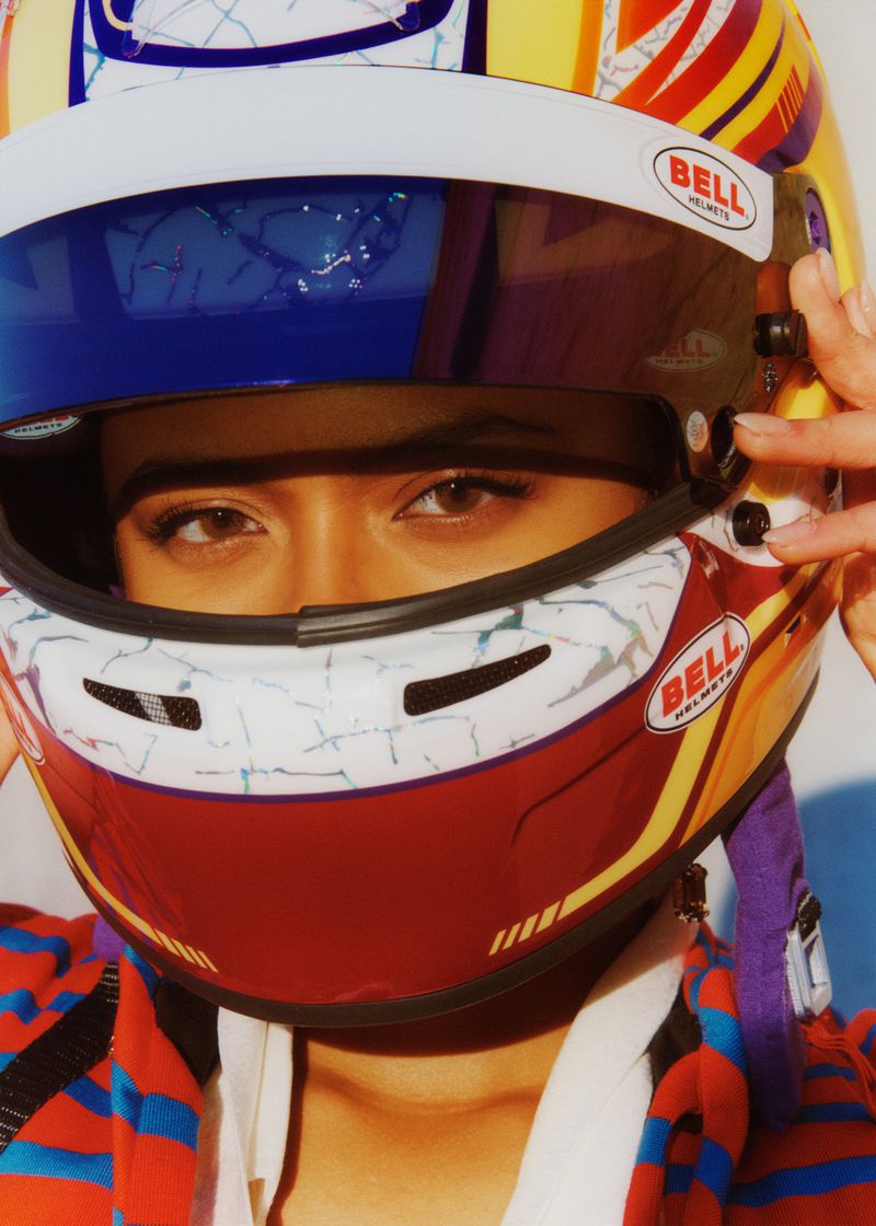 Close up portrait of a person wearing a colourful Bell motorcycle helmet, striped top. Bright studio light.