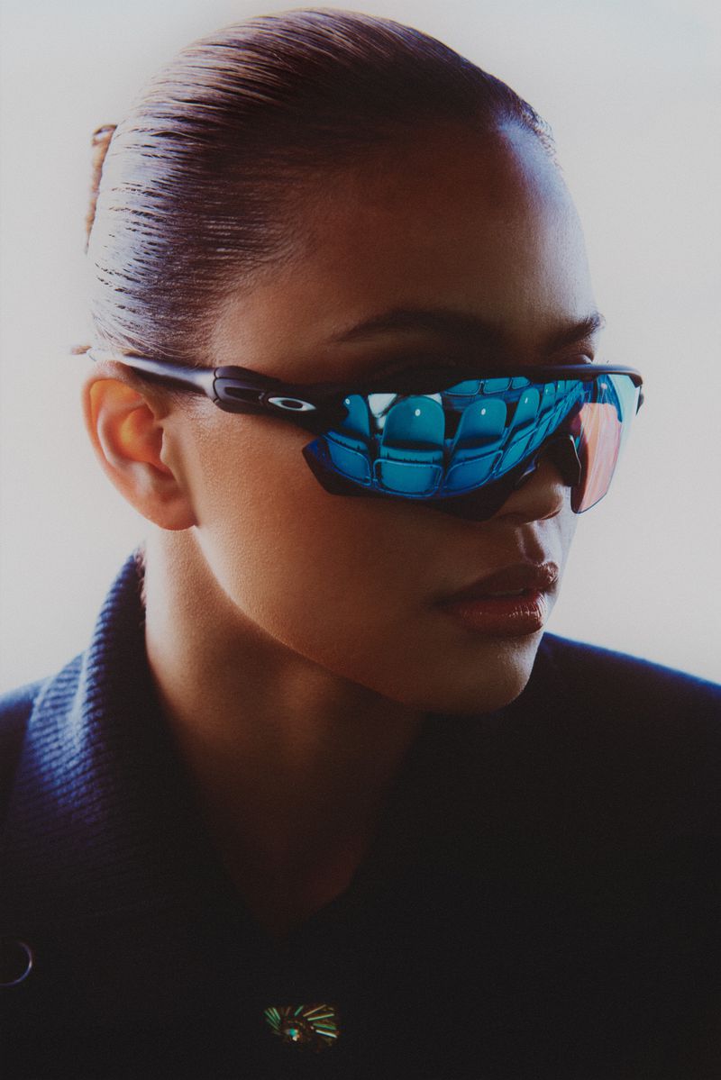 Close-up of a woman with her hair pulled back, wearing black sunglasses with a blue reflection of stadium seating in the lenses.