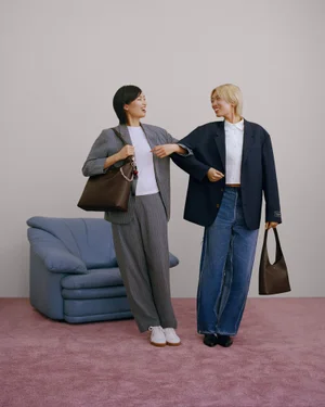 Two models standing on pink carpet in studio setting holding leather handbags for Coach campaign