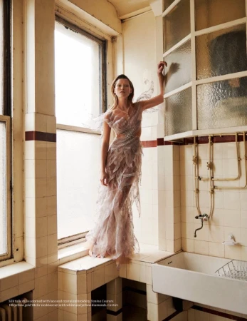 A fashion shot features a model in a light-colored gown with sheer and feather-like details, posing in a tiled bathroom interior space.