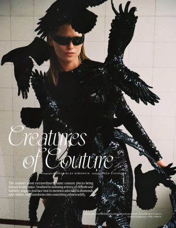 Editorial shot of a model in a black couture dress with bird-like adornments, wearing sunglasses, against a white tiled background.