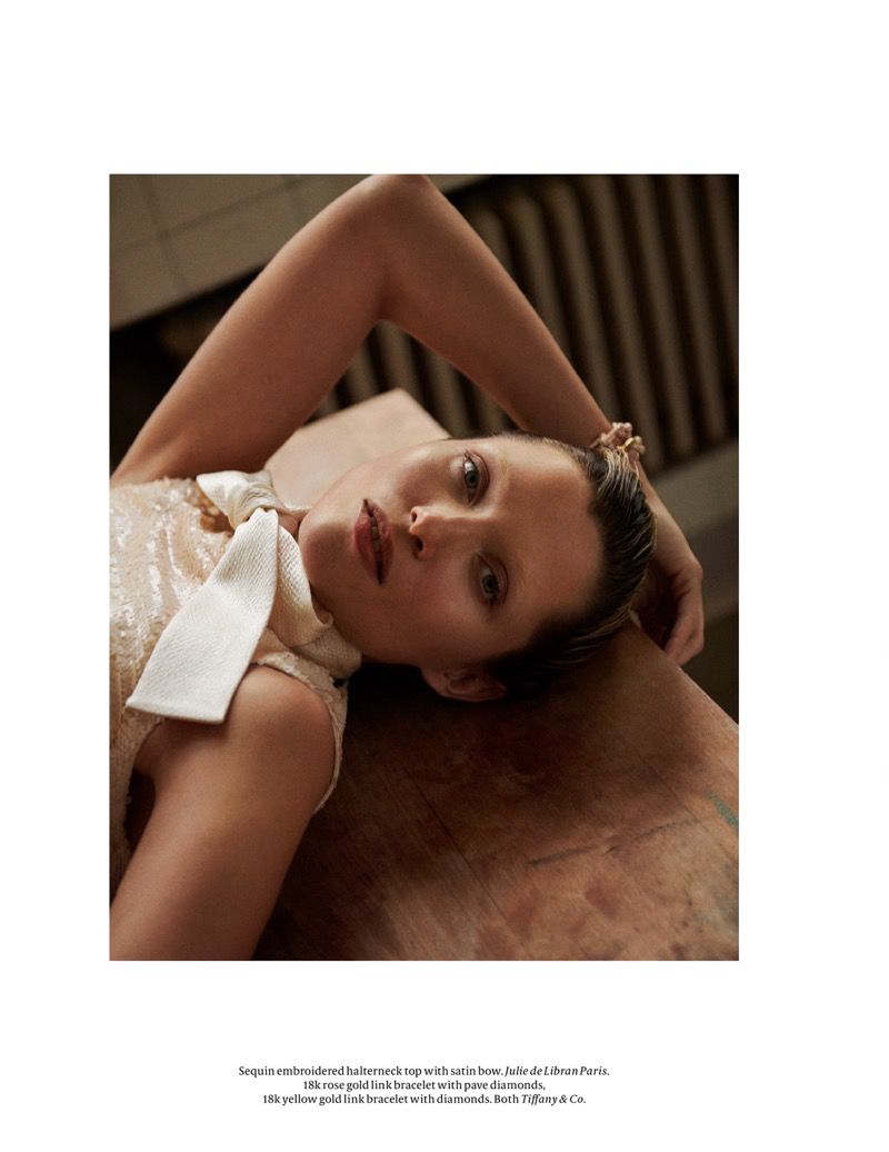 Portrait of a woman wearing a sequin halterneck top with a satin bow, lying on a wooden surface in an indoor setting with warm lighting.