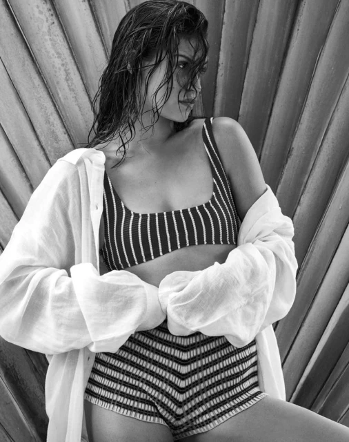 A monochrome shot featuring an adult woman in striped swimwear and a white cover-up, leaning against a textured fan-shaped background.