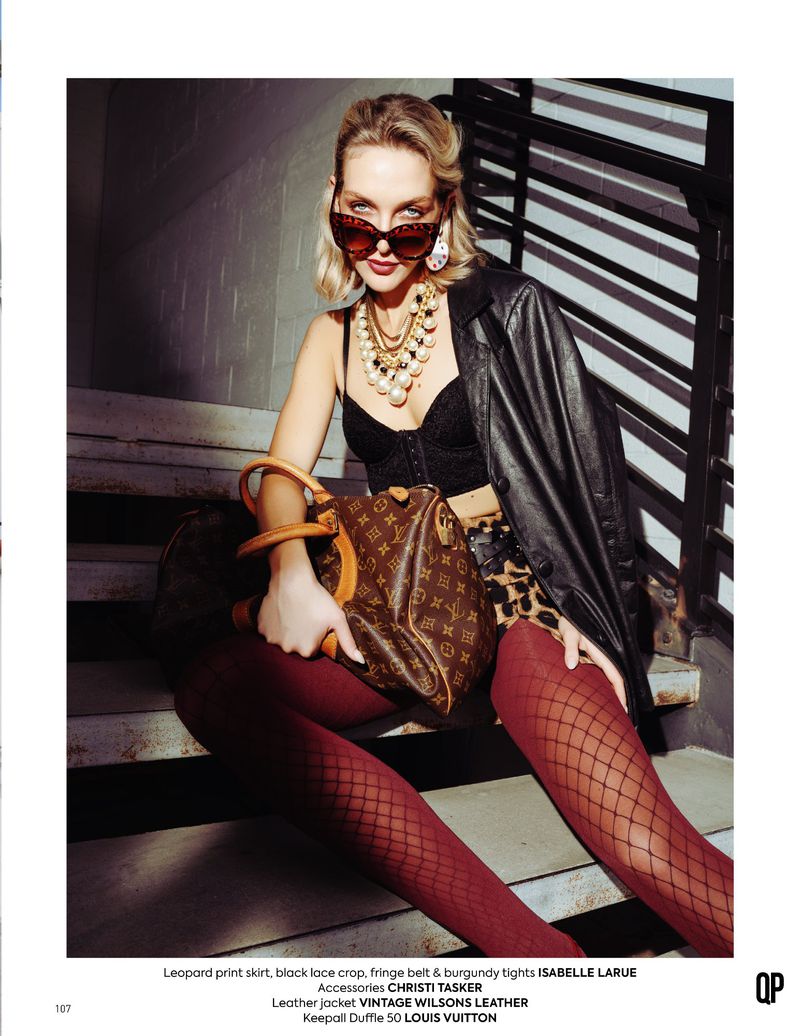 Fashionable blonde woman in leopard print and burgundy tights poses with a Louis Vuitton Keepall Duffle bag on concrete steps.