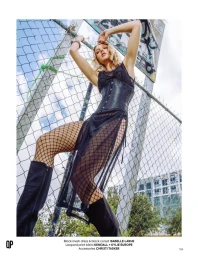 Model in black mesh dress and corset posing against a wire fence outdoors for QP Magazine editorial.