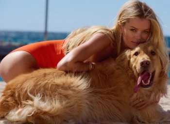 Frida Aasen in an orange one-piece swimsuit lying on a sandy beach embracing a golden retriever.
