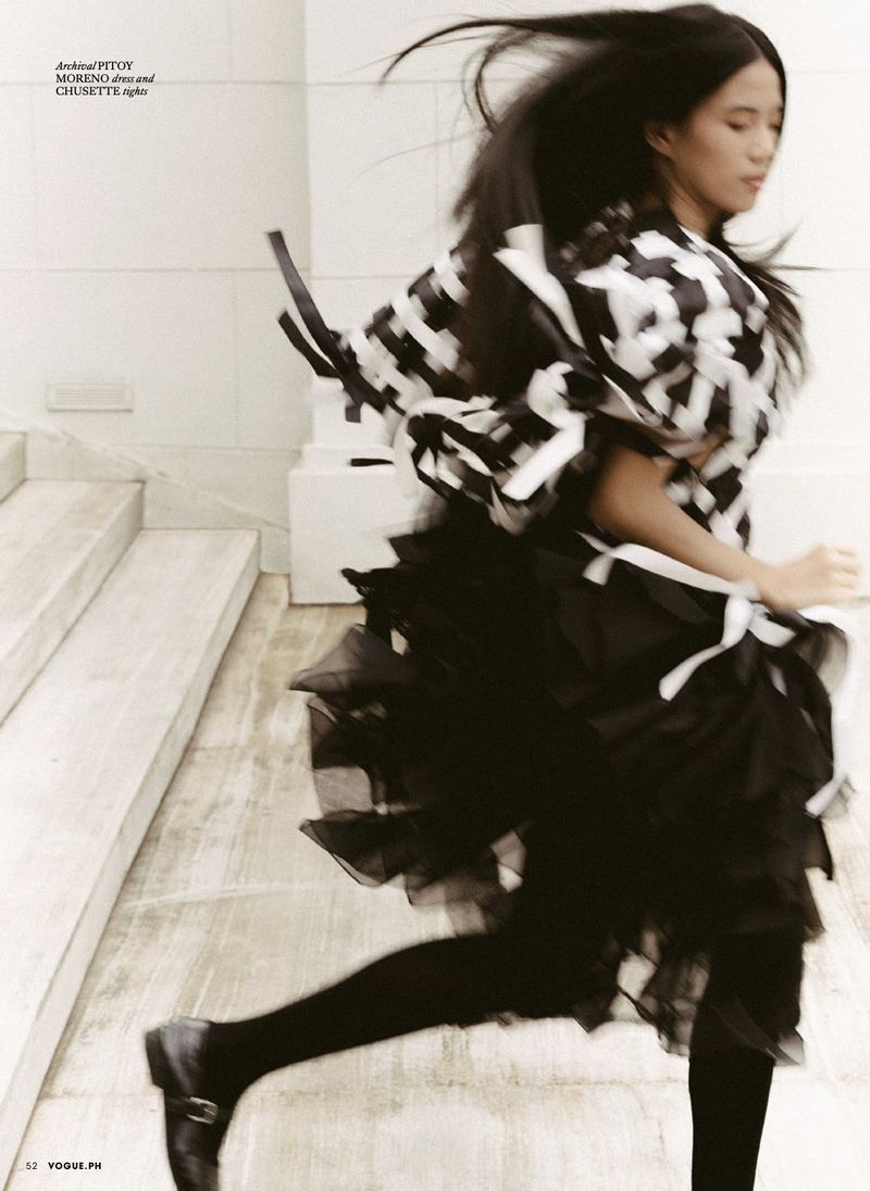Woman in black-and-white patterned top and black tutu runs down steps in blurred motion, legs and black flats visible.