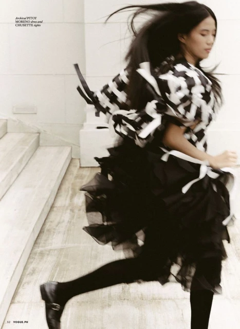 Woman in black-and-white patterned top and black tutu runs down steps in blurred motion, legs and black flats visible.