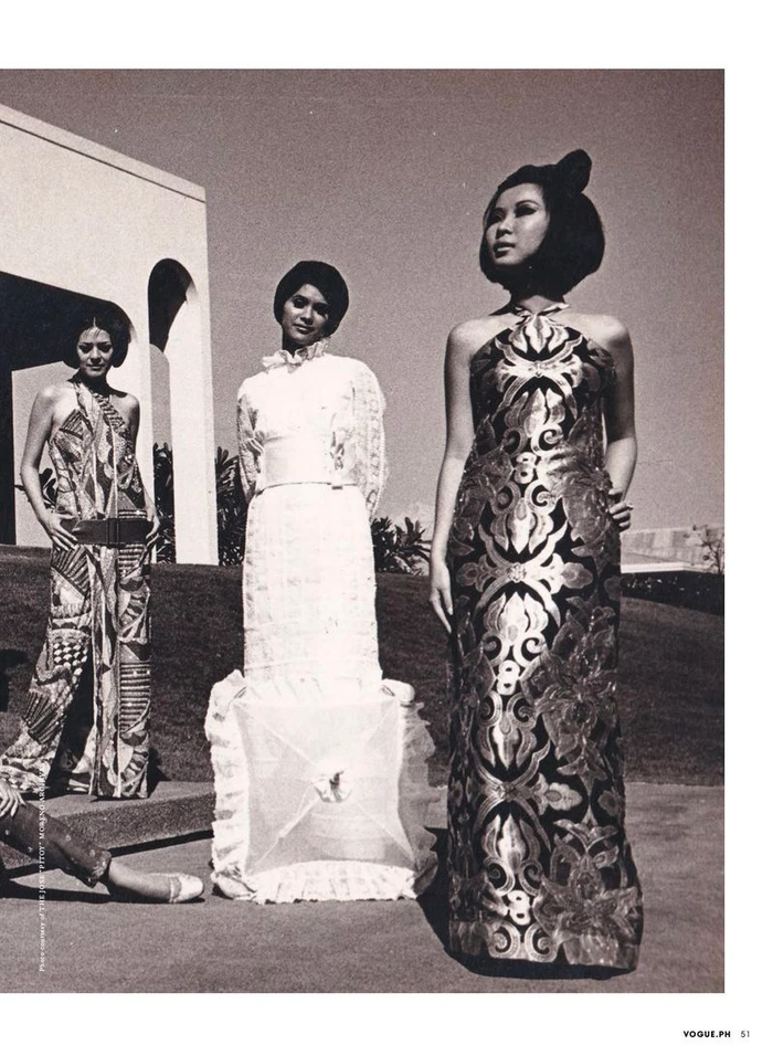 Three models pose outdoors in patterned and ruffled evening gowns with sculpted hairstyles in front of an arched building.
