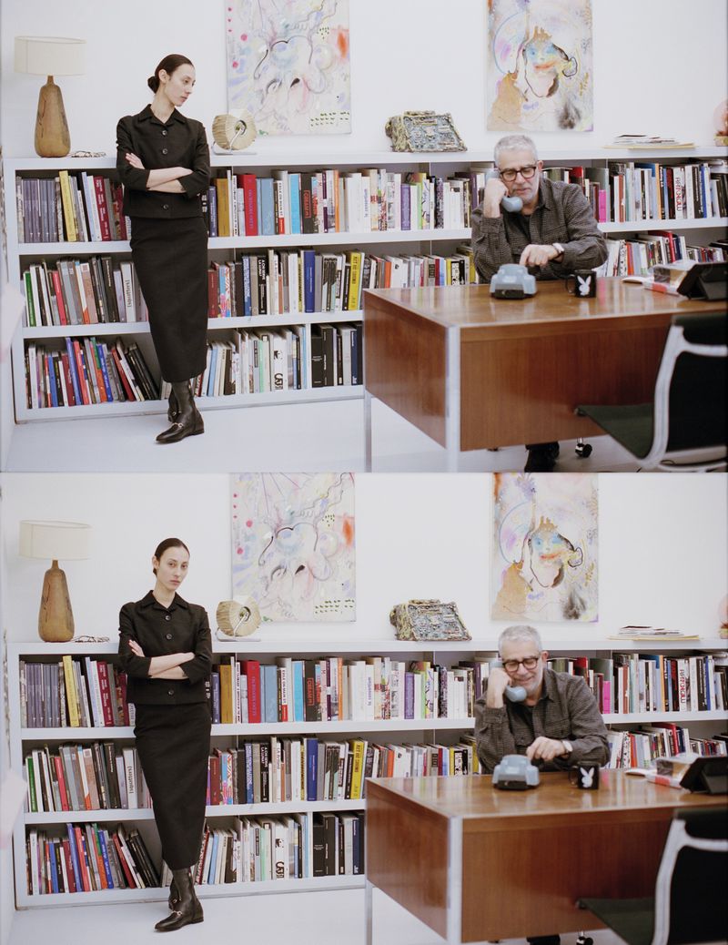 Image of a woman posing in a dark suit next to a bookshelf and a man talking on the phone at a desk in an indoor office setting.