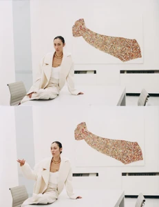 Model Gaia Orgeas wearing an off-white oversized suit and gold necklace seated on a table in a minimalist white room.
