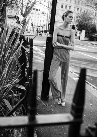 Black and white portrait of a fair-skinned woman wearing pants and a strapless top standing on a city street with arms crossed.