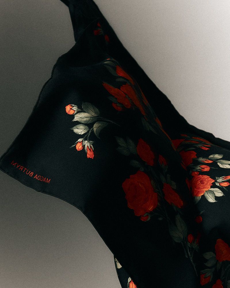 Elegant black silk scarf with vibrant red rose floral pattern, draped against a soft, neutral background in a gentle, flowing composition.