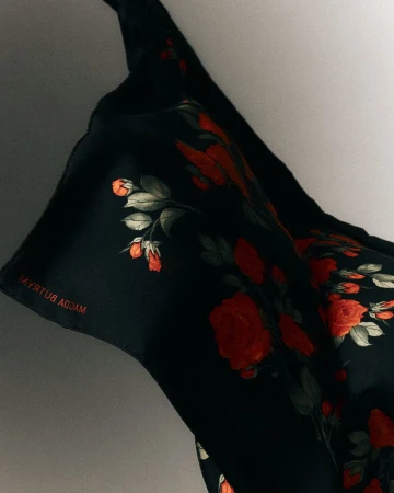 Close-up of black silk fabric featuring a red rose print and Magda Butrym branding against a neutral background.