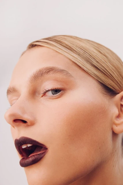 Close-up portrait of a woman with dark lipstick against a plain background. Beauty shot emphasizing makeup and facial features.