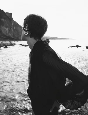 Model Maaike Klaasen in a dark sheer top standing by a rocky coast for Numéro Switzerland, photographed by Xavi Gordo.
