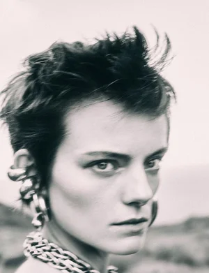 Close-up portrait of a model with short dark hair wearing chunky silver earrings and a braided silver chain necklace.
