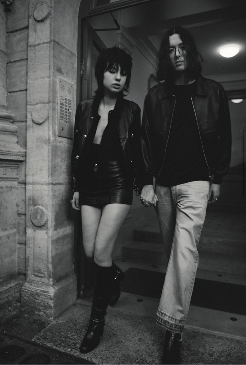 A stylish monochrome portrait of a couple standing in an urban setting, the woman in a leather skirt and boots, the man in jeans.