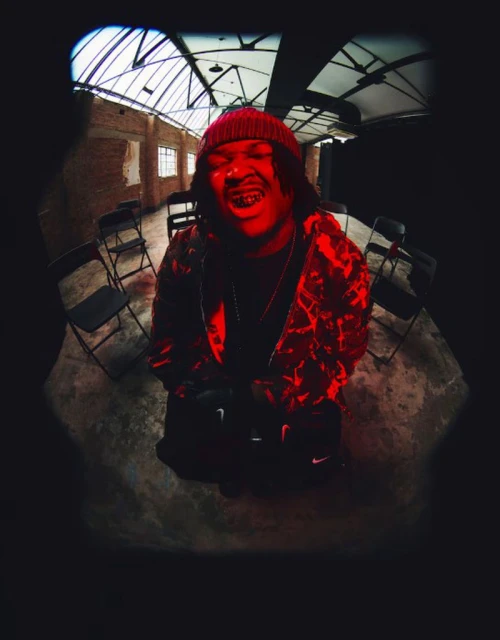 Adult male portrait in photo studio with dramatic red lighting wearing a beanie, patterned hooded jacket and dark colored pants and sneakers.