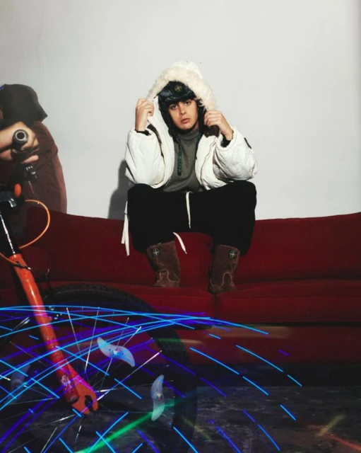 Teen sits on red couch wearing winter gear. A person with a bicycle and long exposure light trails are visible.