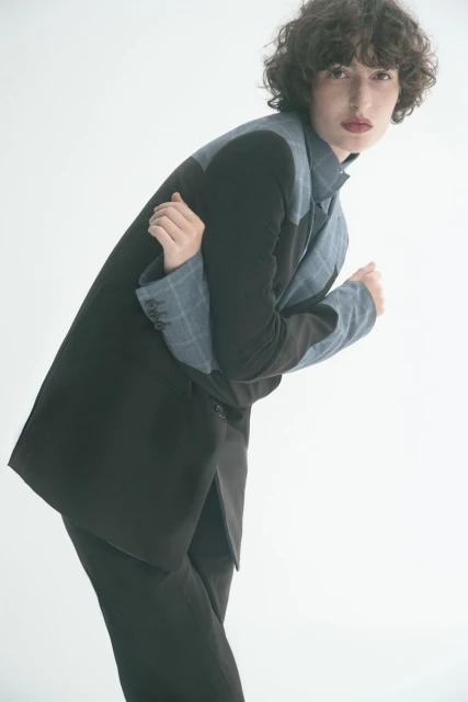 Adult woman in a studio, wearing an oversized black and blue blazer, arms crossed, looking at the camera. Fashion shot, studio lighting.