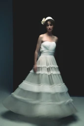 Woman wearing a strapless white layered gown and a floral hairpiece against a dark backdrop